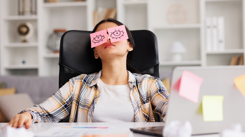 Woman sleeping at desk with open eye drawings covering her eyes