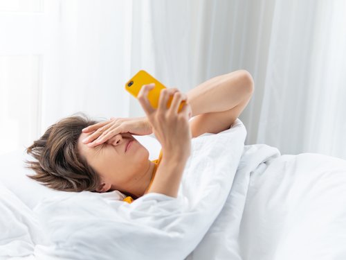 Sleepy woman looks at smart phone