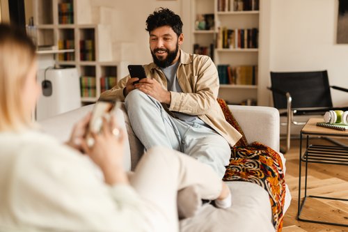 Couple sitting on sofa typing on cellphones